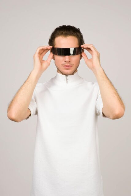 A young man in a stylish white shirt poses with futuristic VR glasses, embodying modern tech fashion.