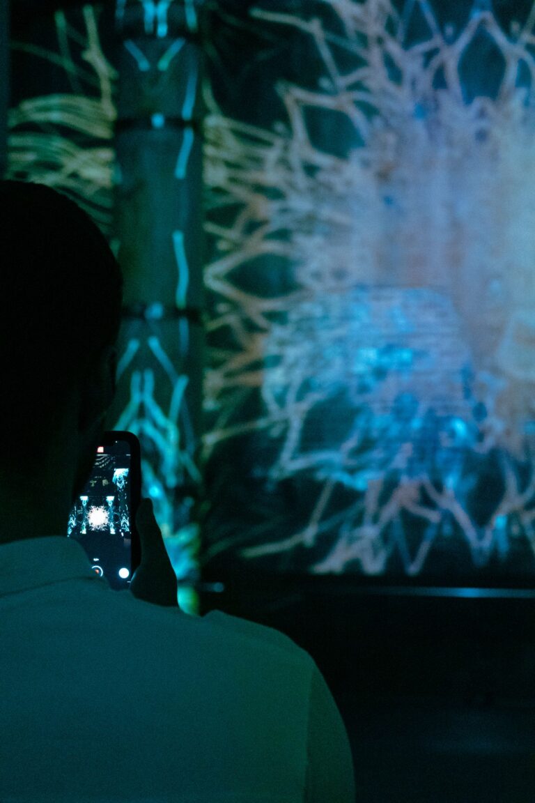 A person photographing a vibrant digital art installation using a smartphone at night.