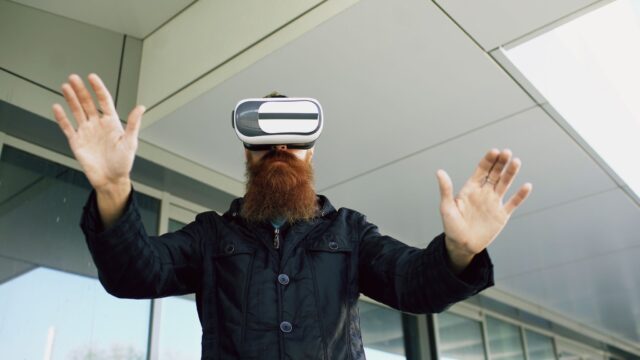 Bearded man wearing VR headset interacts outside modern building. Experiencing virtual reality.