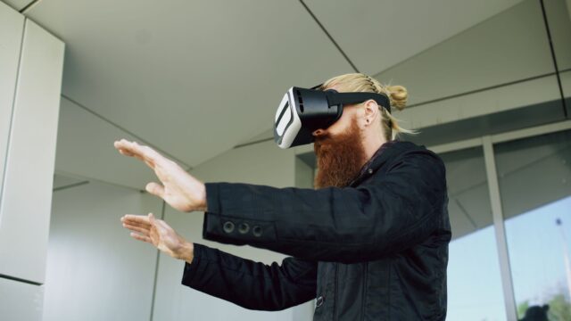 Side view of a bearded man interacting with VR headset outside modern building.